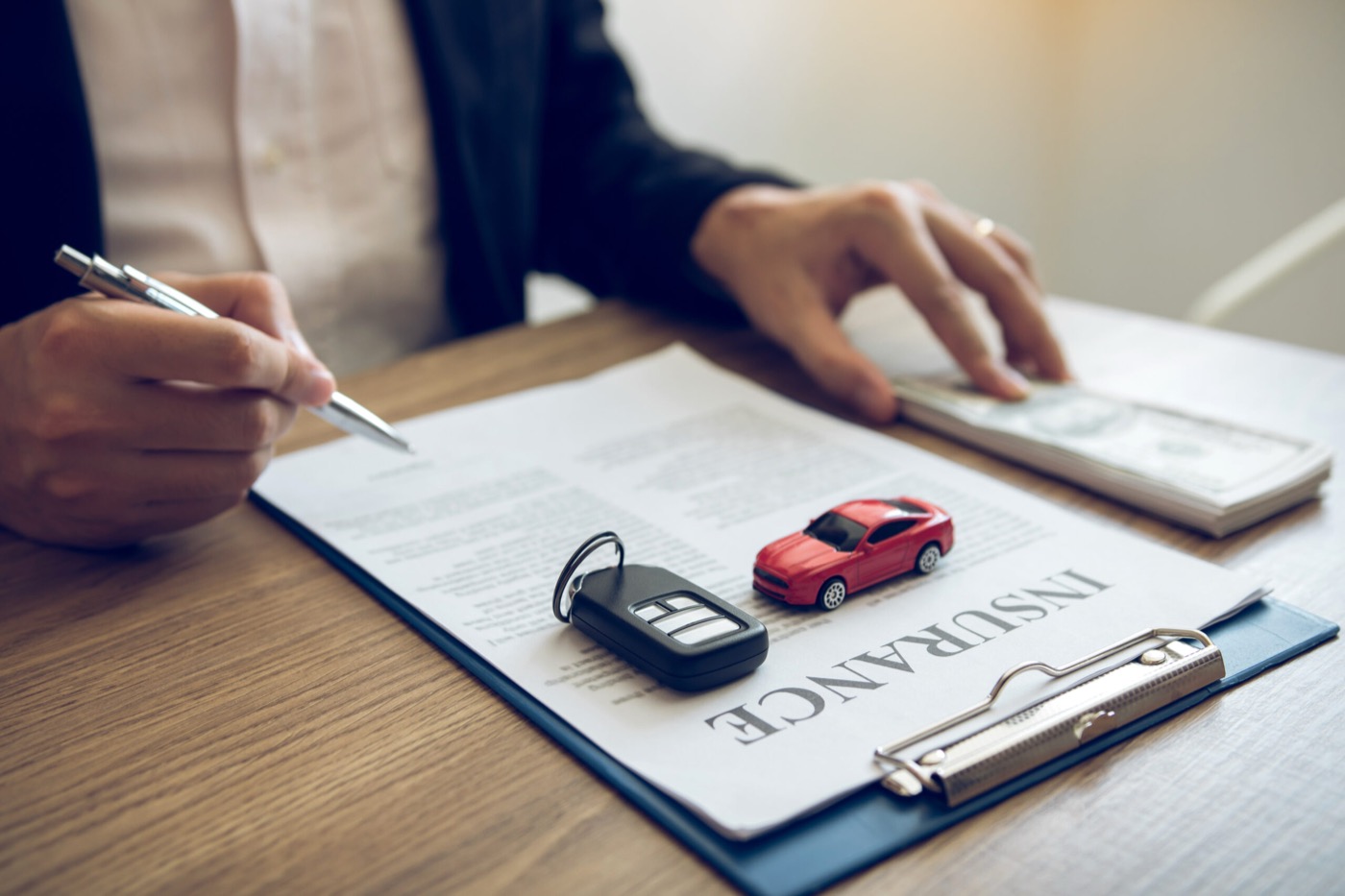 Agent is signing the Auto insurance contract for the car at the document on the desk.
